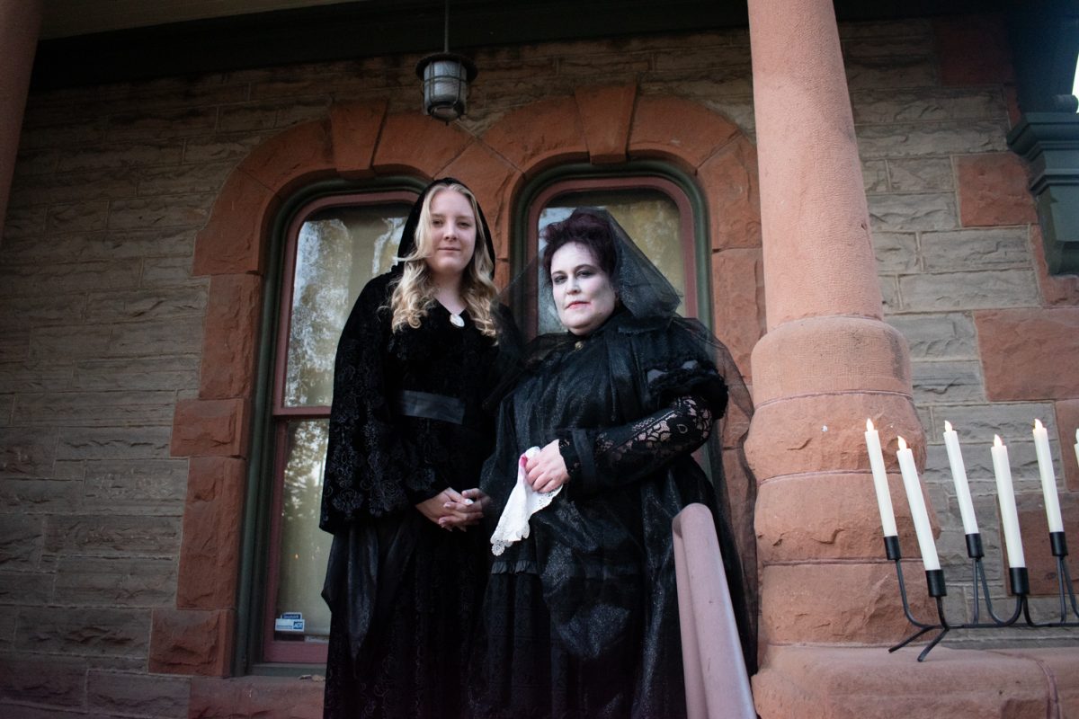 Two women stand infront of a house wearing all black costumes.