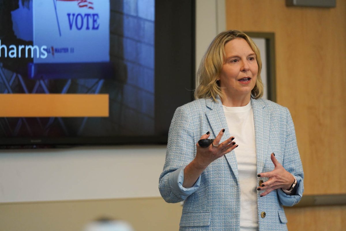 A woman in a blue blazer stands and talks.