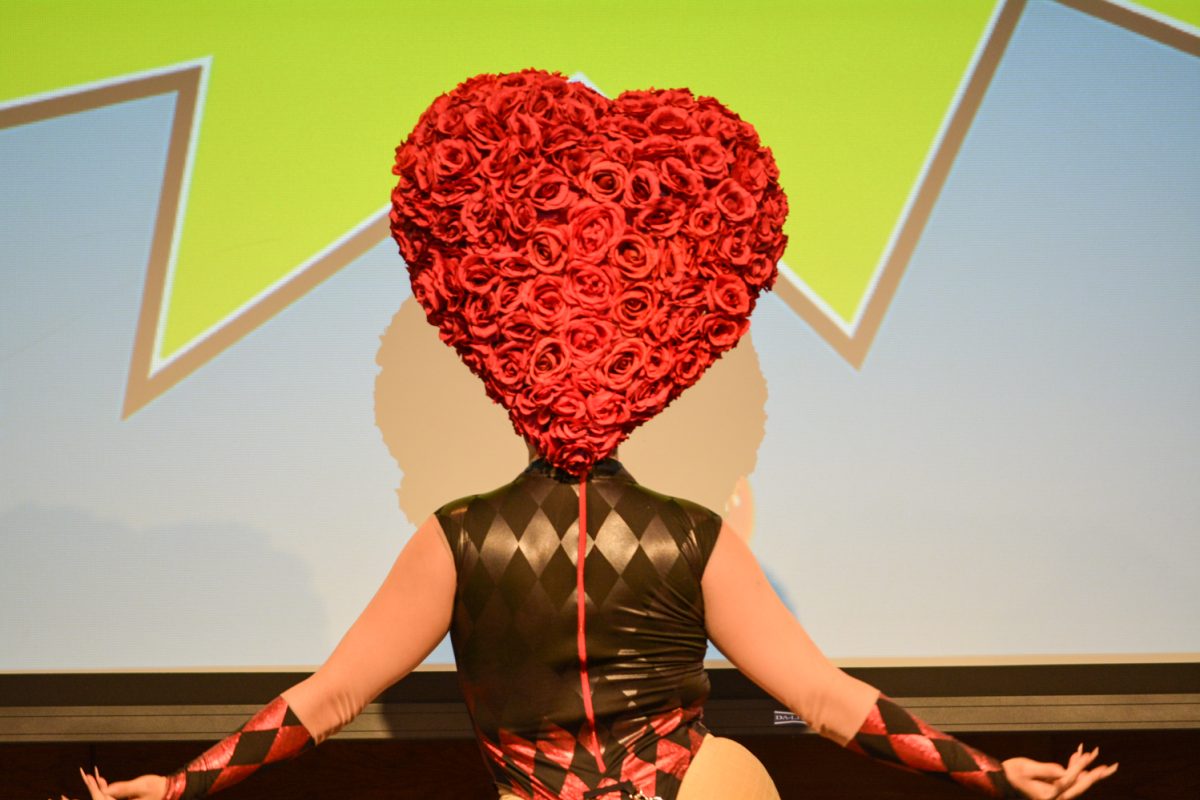 Performer in a black and red bodysuit with a heart shaped rose headpiece