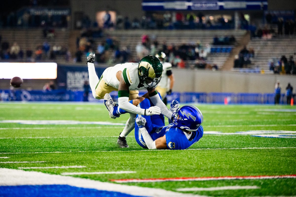 A football player in white and green lands on top of a player in blue and white.