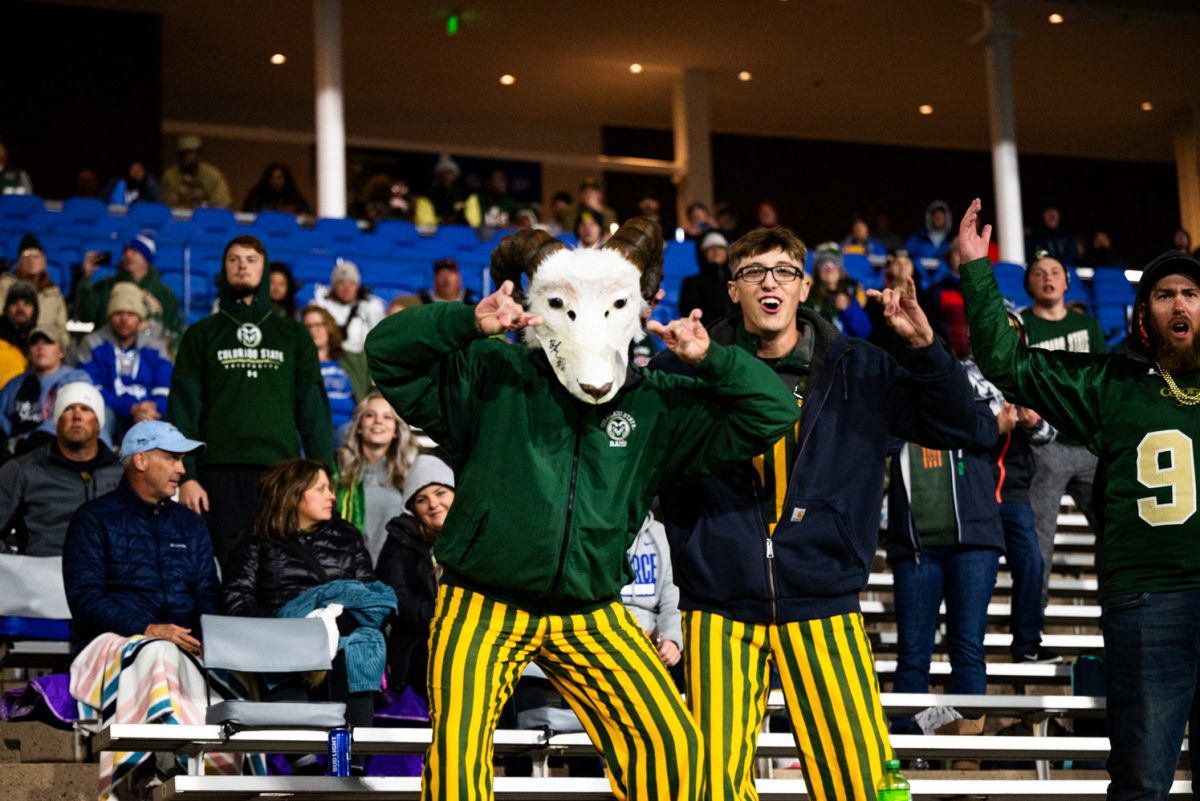 Two football fans in green and yellow-striped overalls hold up ram horns. One is wearing a ram mask over his head.