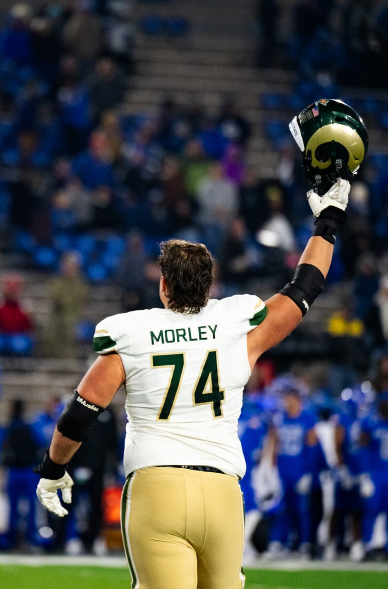 A football player in white and green holds his helmet in the air.