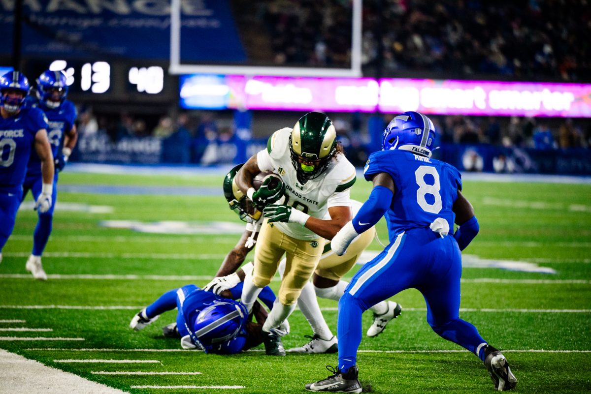 A football player in white and green runs with a football at a player in blue and white.