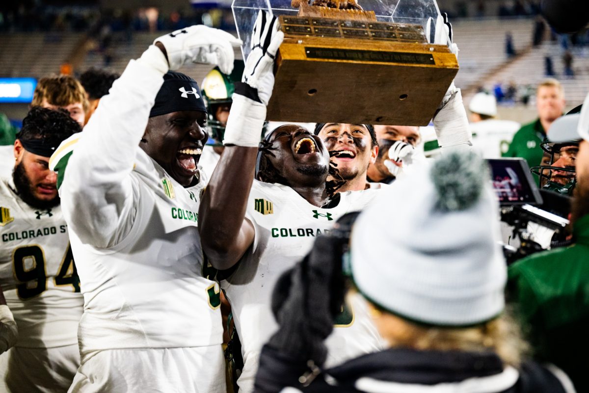 Football players in white and green hold a trophy in a case aloft while cheering.