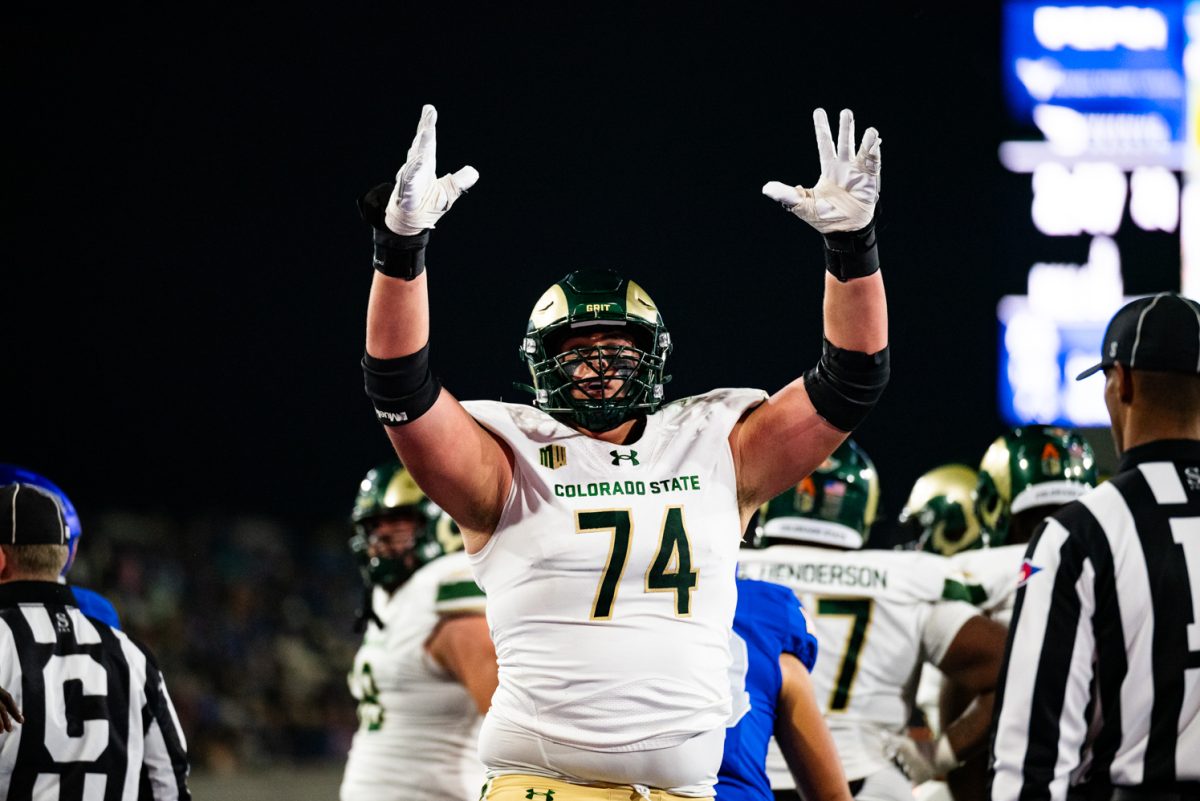 A football player in white and green raises his arms in the air.