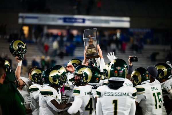 A crowd of football players in white and green hold up a bronze trophy in a glass case.