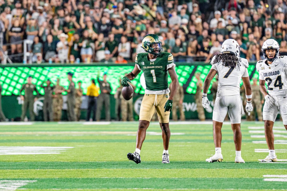 A football player in a green and gold uniform walks across the field while holding the tip of the football in one hand.