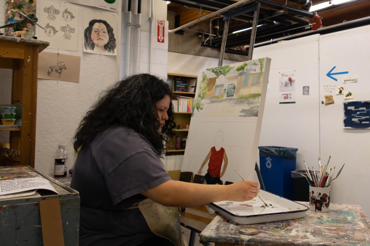 woman with black curly sits in an art studio and works on portrait of a young boy infront of a house.