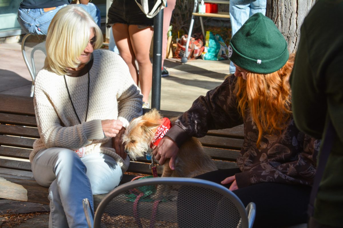 Two women petting a dog with a red bandana