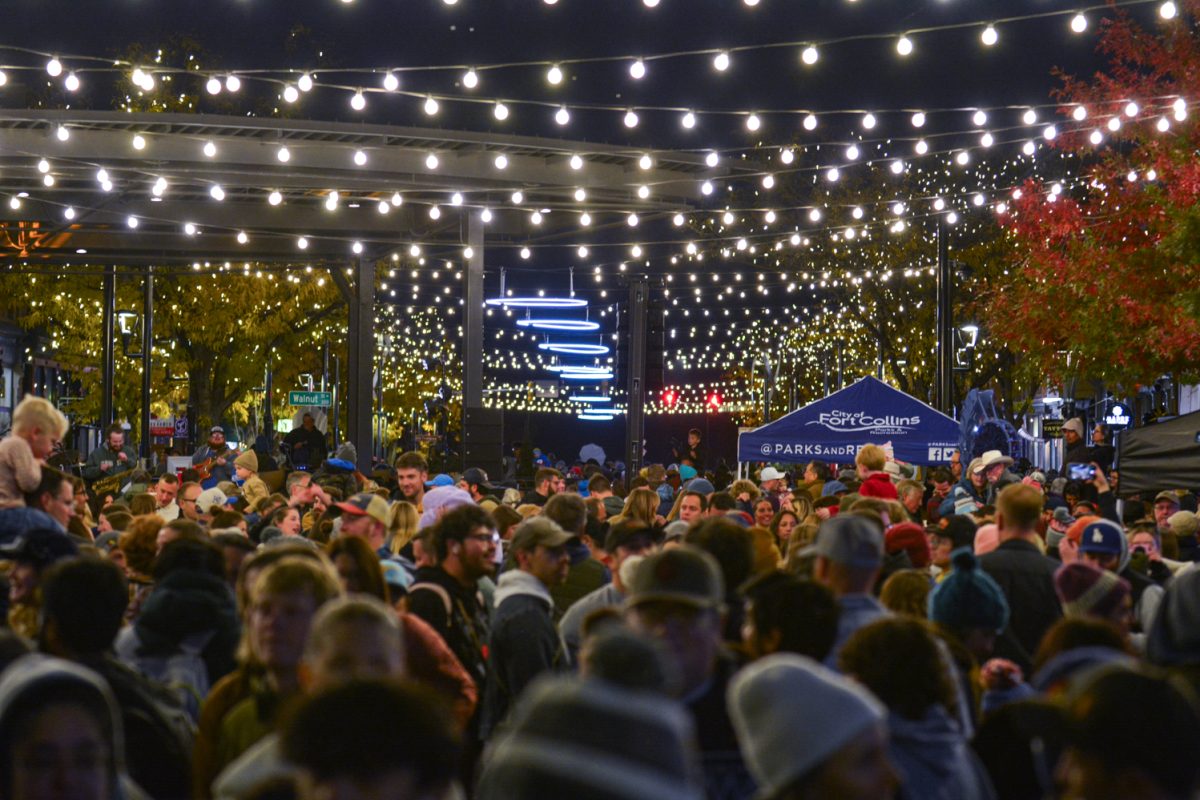 Crowds of people stand around with string lights hanging over them.