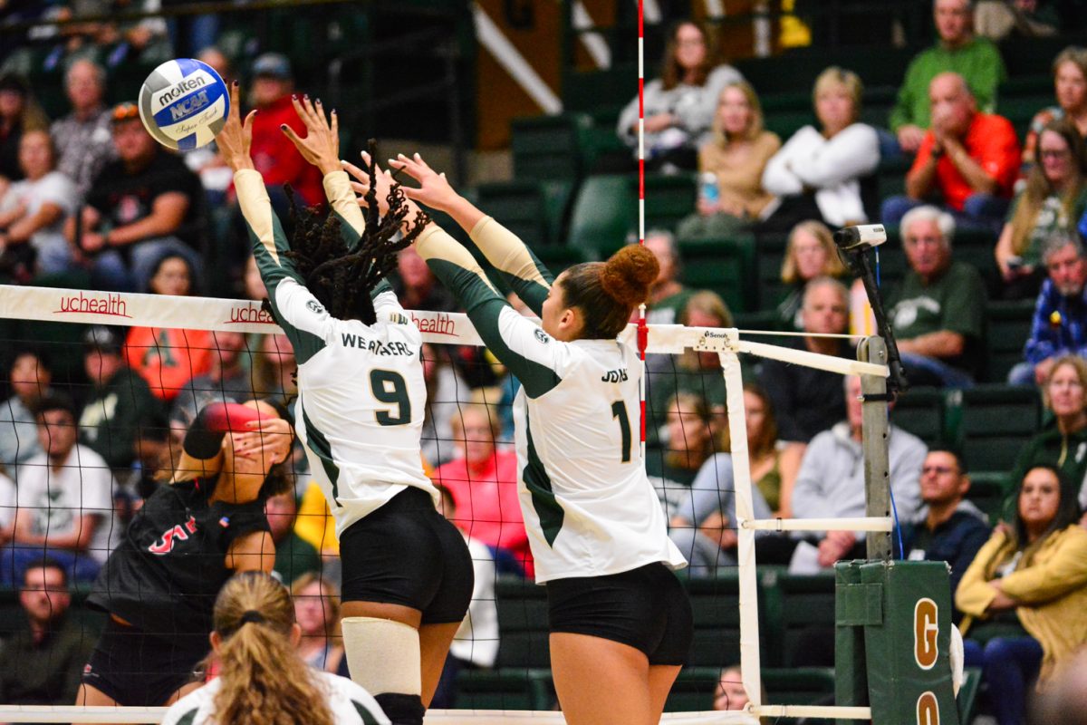 Two girls in green and white jerseys blocking the ball