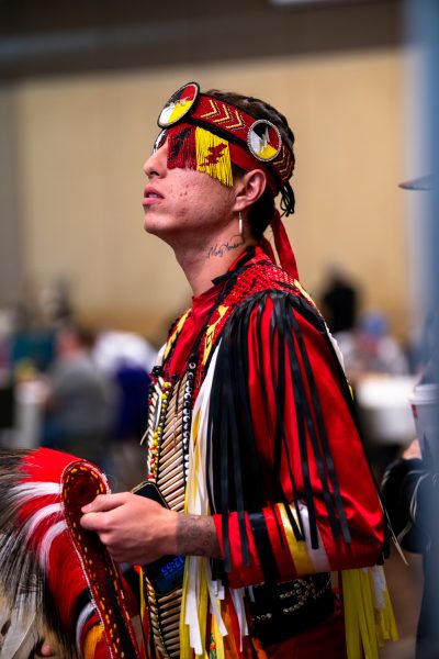 A dancer in traditional Native American regalia with an array of colors dances in a ballroom.