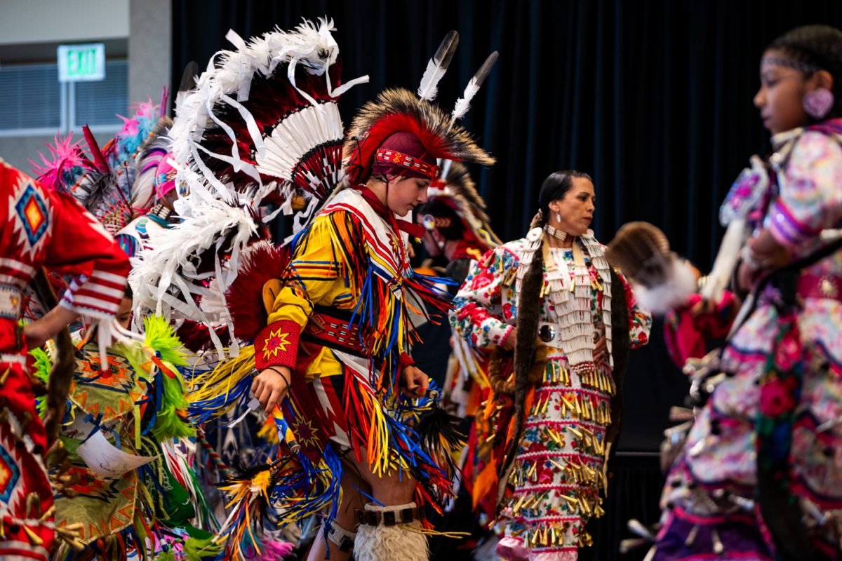 A dancer in traditional Native American regalia with an array of colors dances in a ballroom.