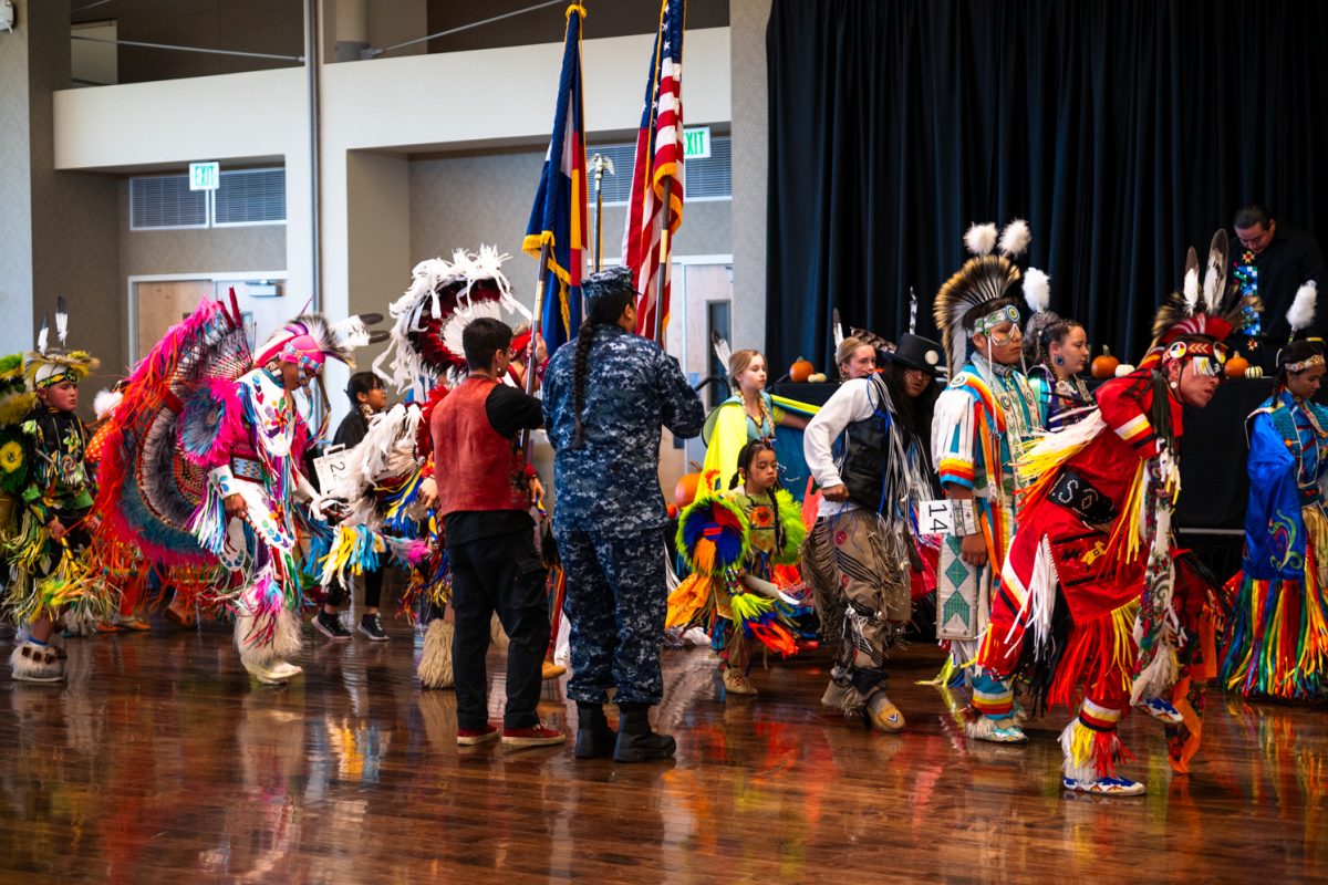 Dancers in traditional Native American regalia with an array of colors dances in a ballroom.