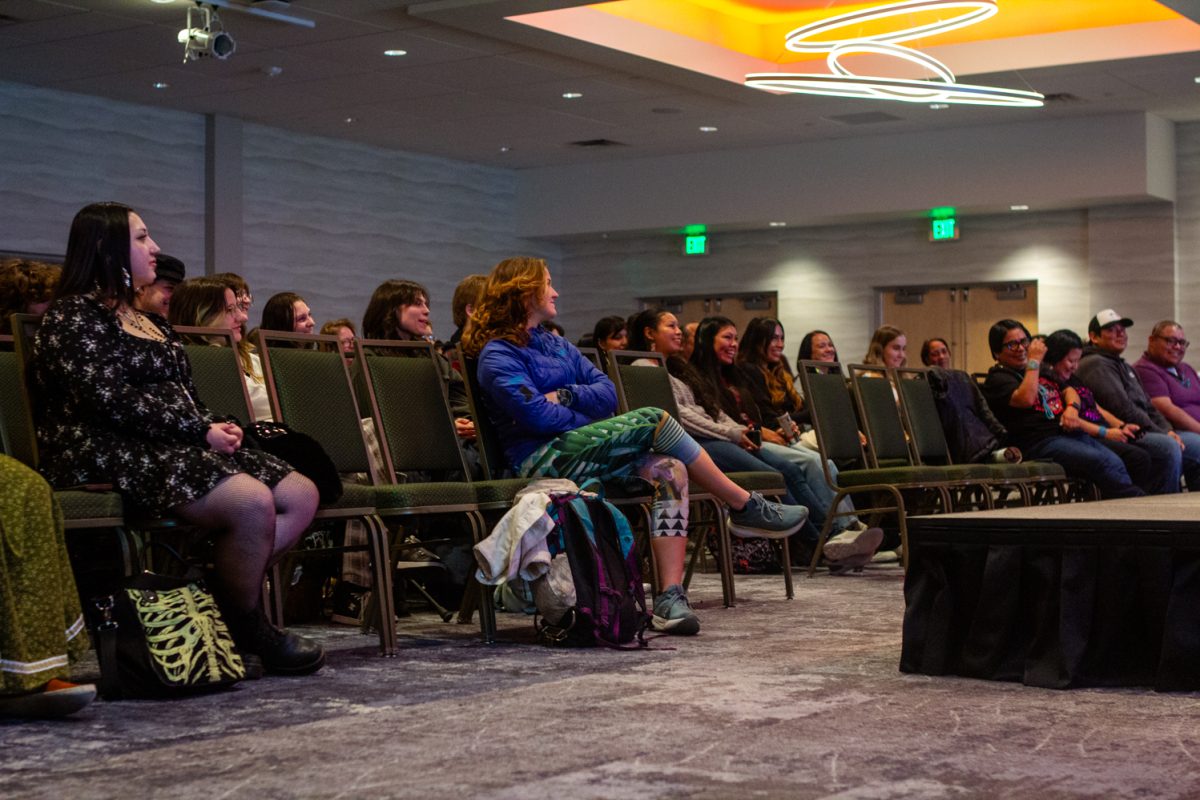 People sitting in chairs in an audience smile and laugh.