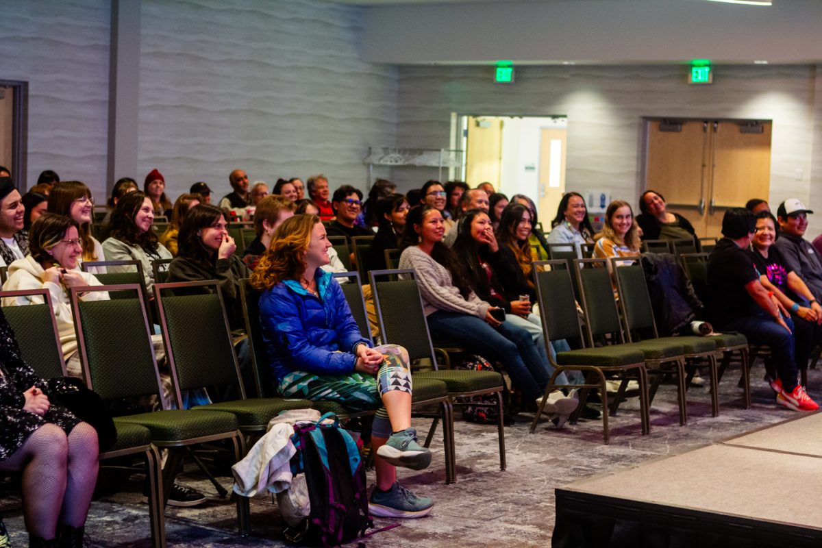 People sitting in chairs in an audience smile and laugh.