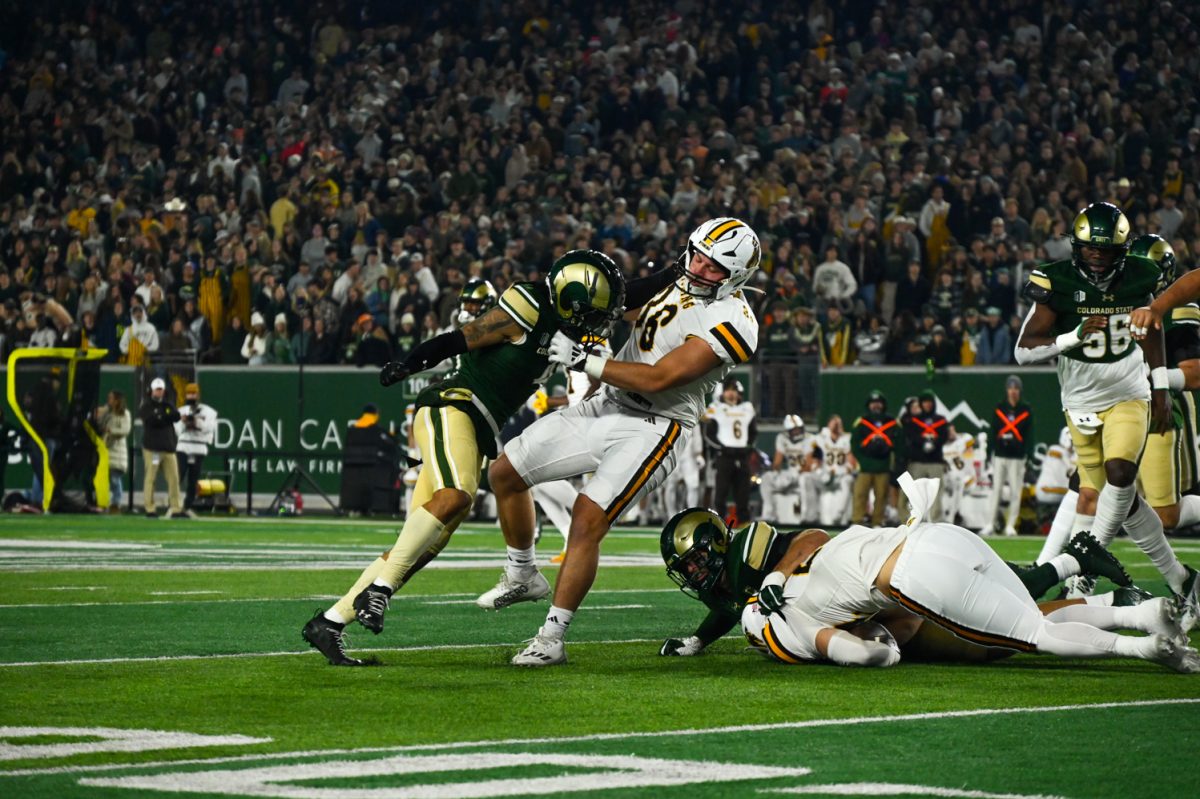 a player in green and gold pushes a player in a white, brown and yellow uniform on the football field