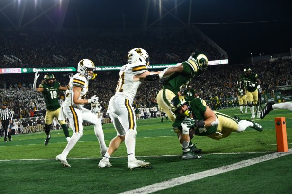 A player in a green and gold uniform dives into the endzone