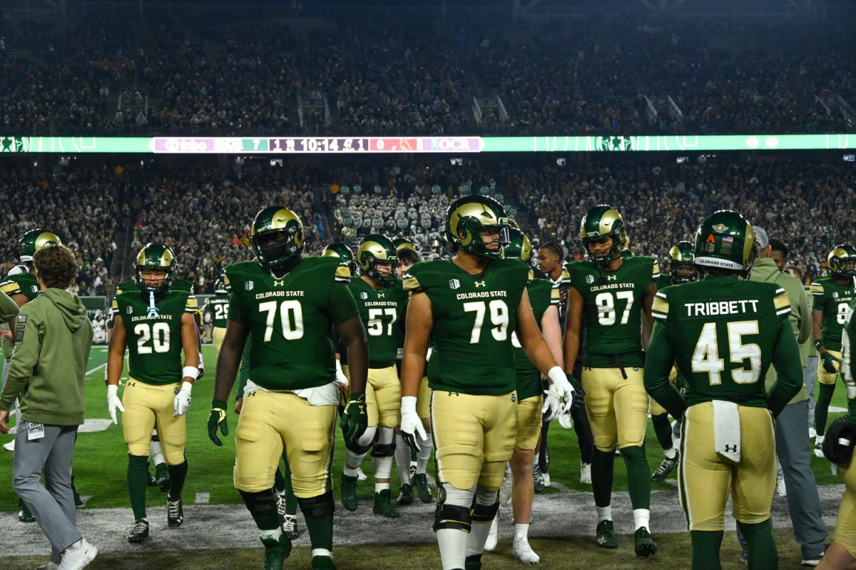 A group of football players in green and gold uniforms walk off of the football field