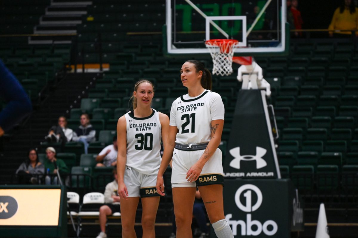 Two female basketball players in white and green talk on the court.