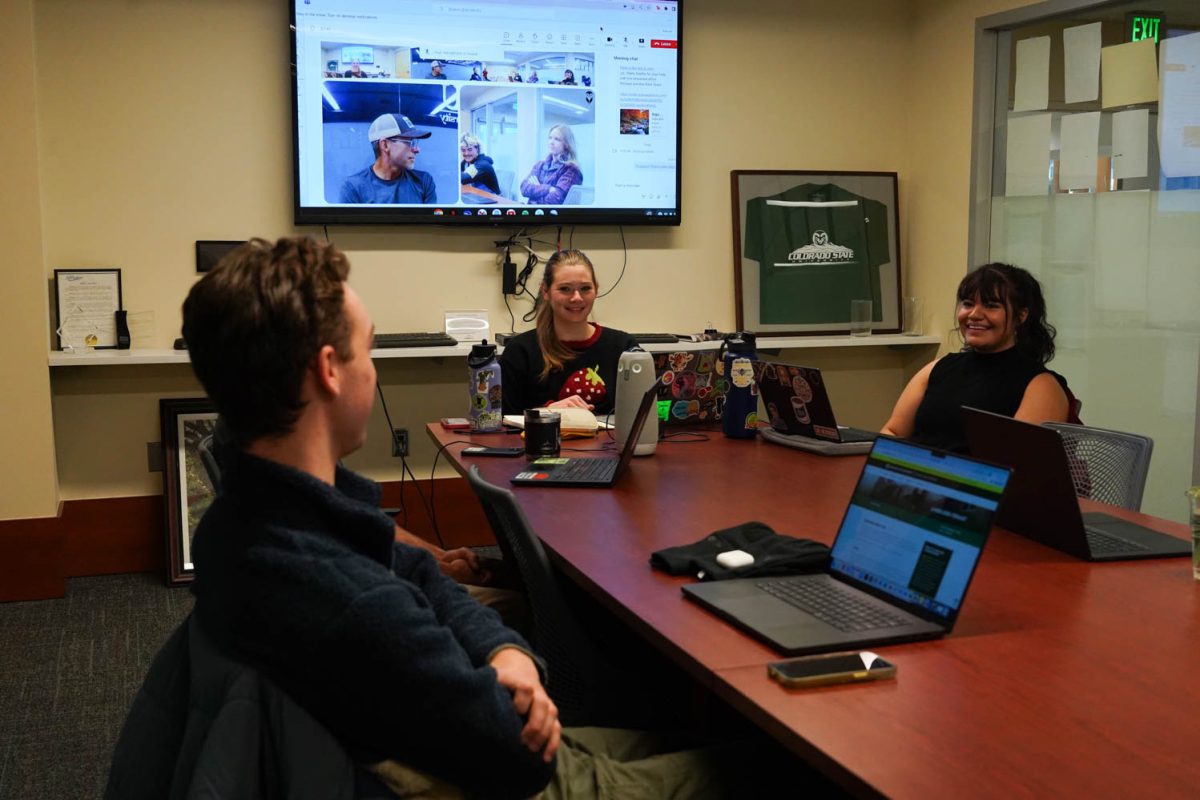 A group of people sit at a conference table with laptops and a screen behind them.