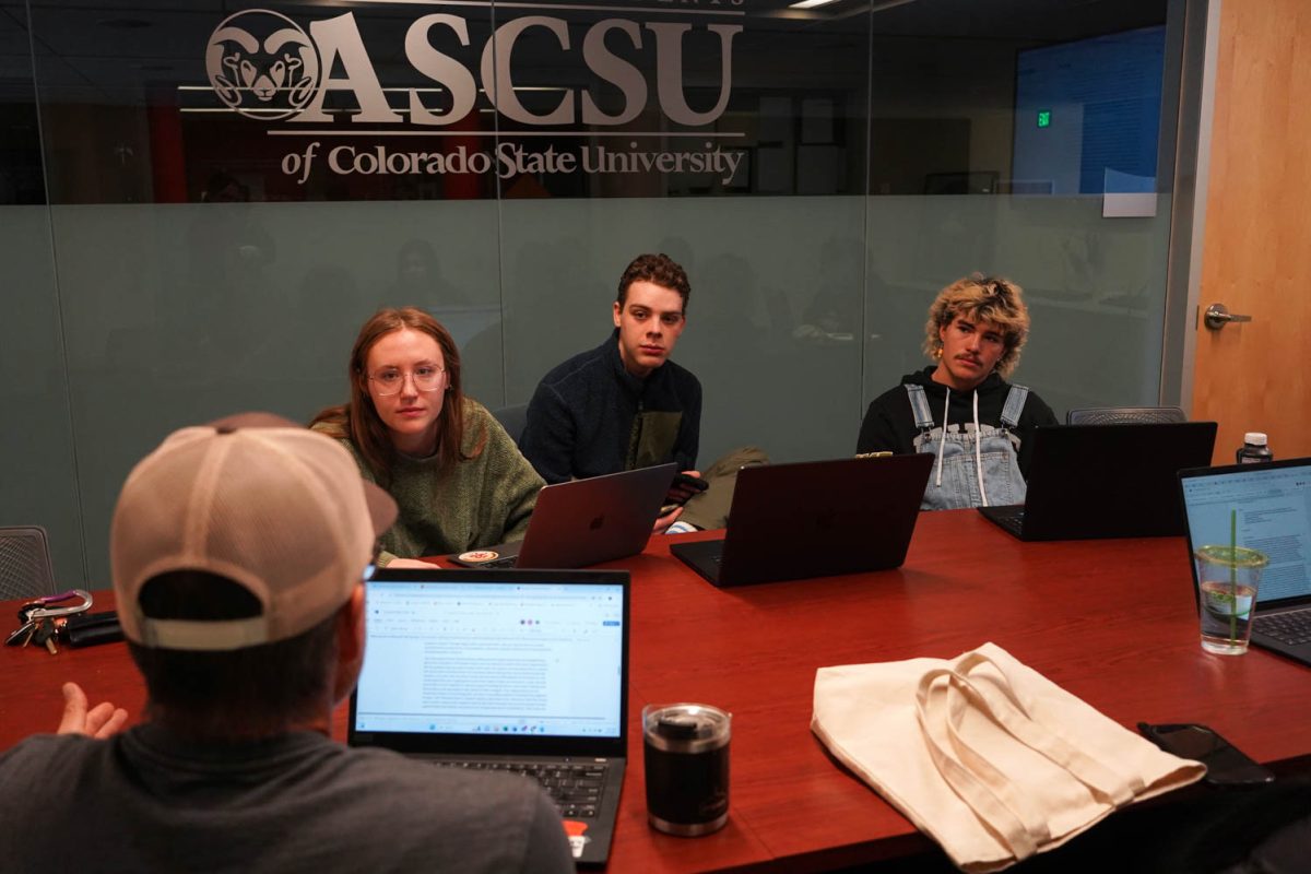 A group of people sit at a conference table with laptops and a screen behind them.