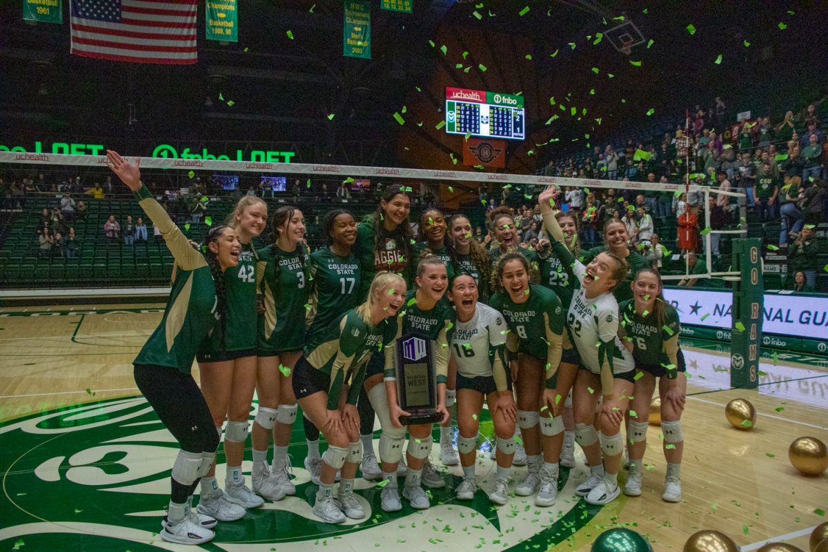 A volleyball team poses with a trophy, with balloons and confetti around them.