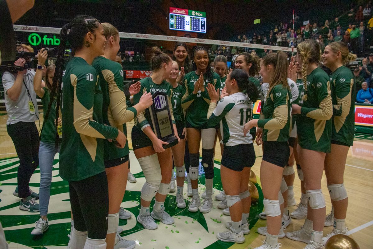 A volleyball team claps and celebrates while holding a trophy.