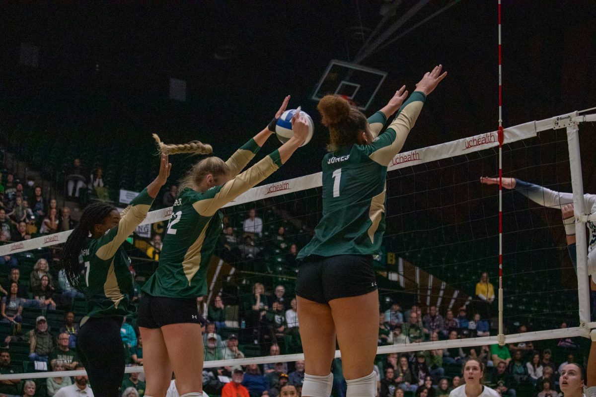 Four volleyball players jump to block the ball.