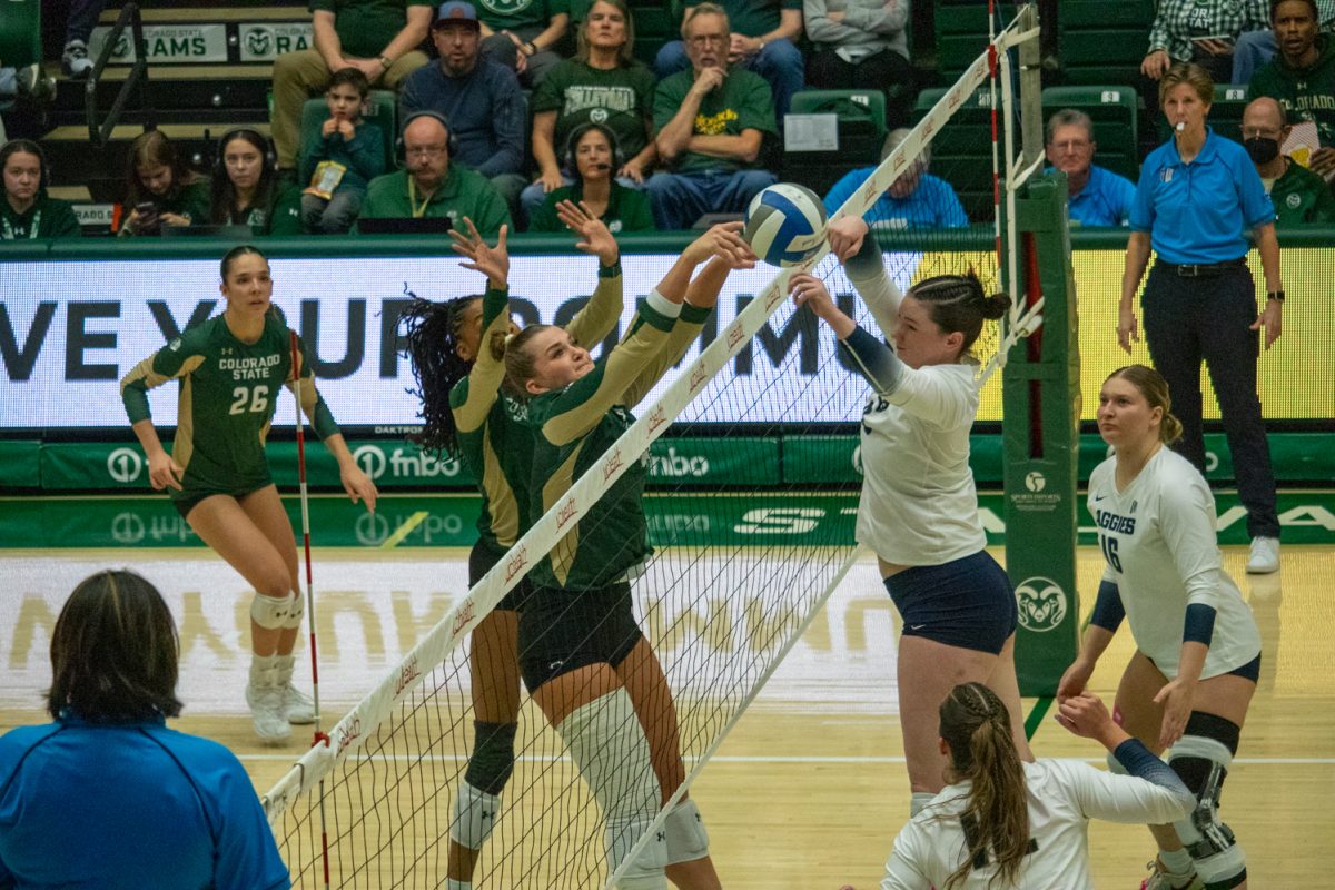 Two volleyball players jump to try to get the ball at the net.