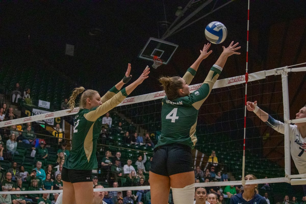 Two volleyball players jump to block the ball being hit by the other team