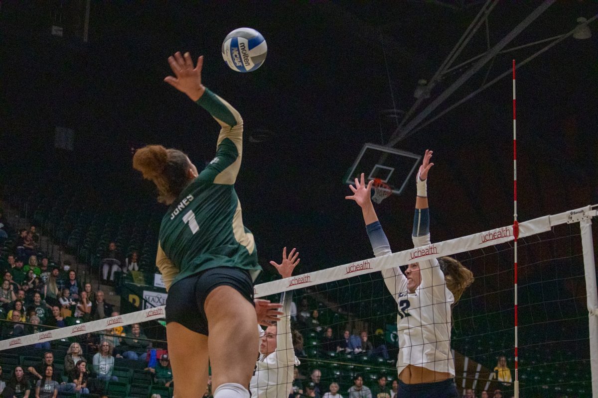 A volleyball player hits the ball while the other team tries to block.