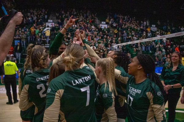 A group of volleyball players cheer in a circle.