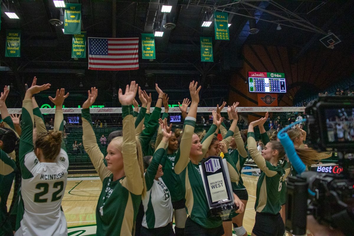 Volleyball players cheer with their hands in the air, one holds a trophy.