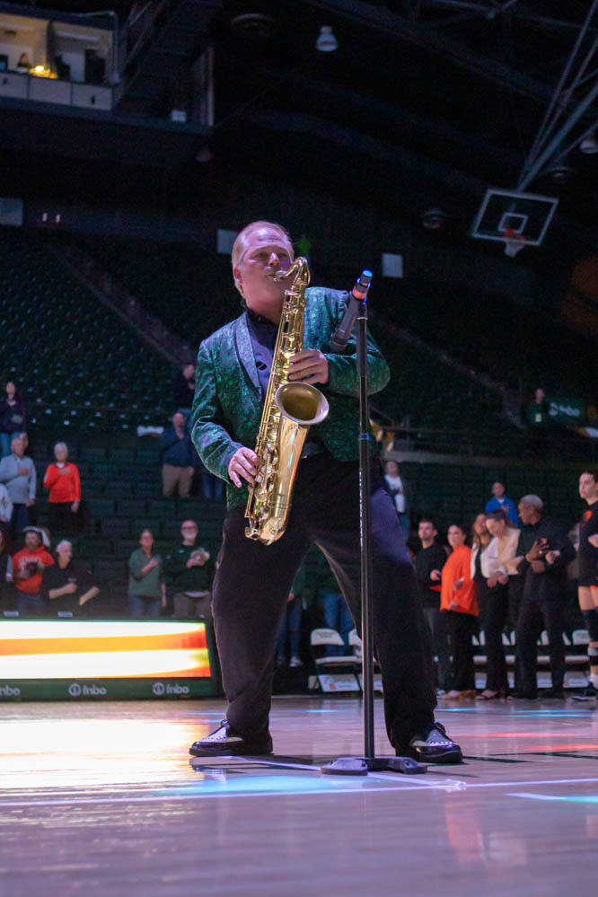 A man in a green suit plays the saxophone in front of a microphone ina large arena.