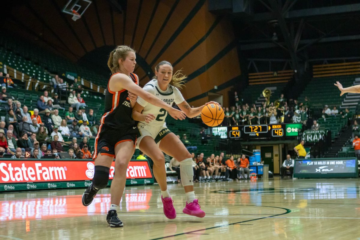 A woman in a white jersey bounces an orange ball at a sporting event while a woman in a black jersey tries to steal the ball.