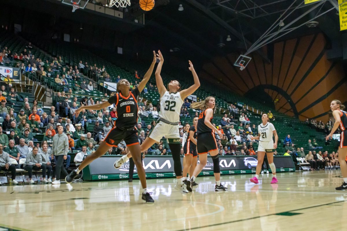 A woman in a white jersey jumps while throwing an orange ball in the air while a woman in a black jersey jumps with her at a sporting event.