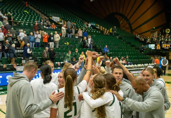 A group of women in white jerseys stand together at a sporting event with their hands in the air.