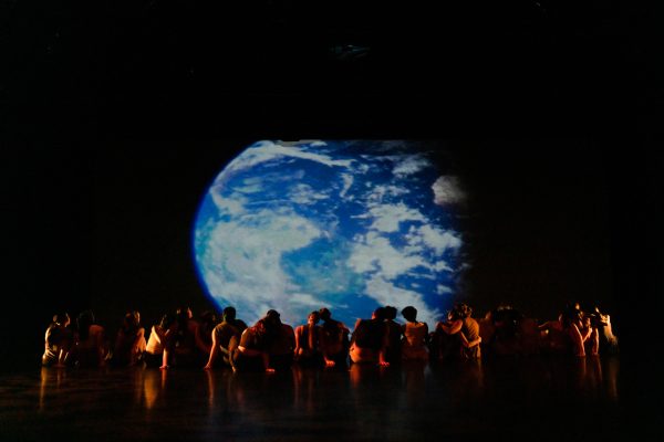 A collection of people sit together watching a projection of Earth on a screen.