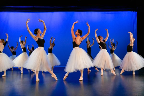 Dancers in black tops and white skirts dance on stage.