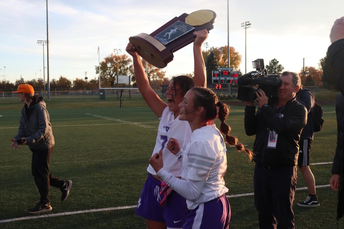 Two players cheer as they hold up the championship trophy.