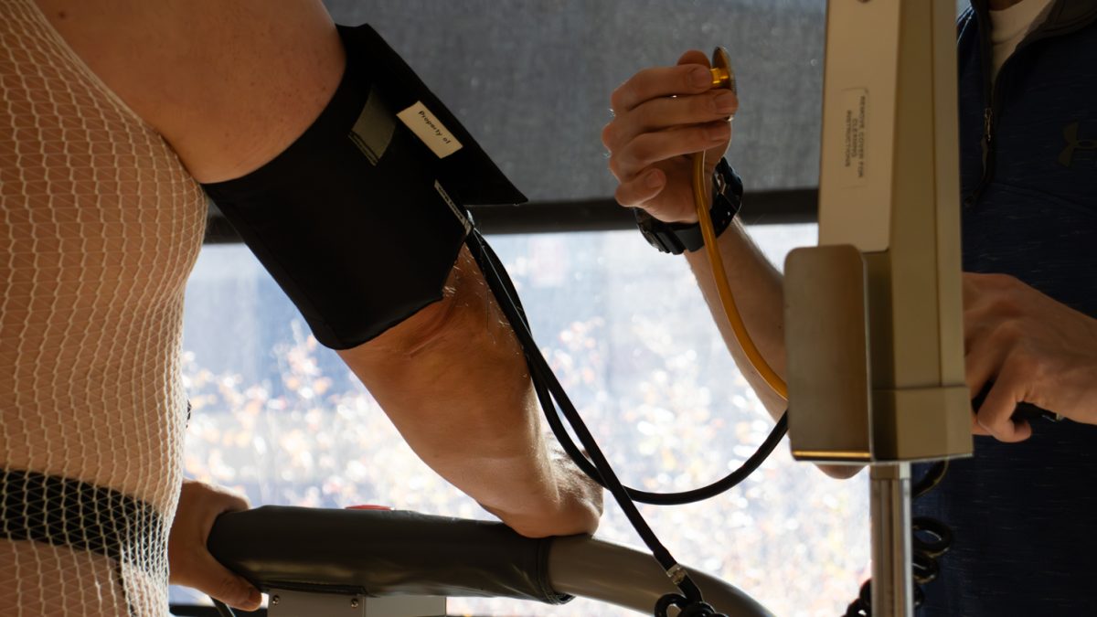 A close picture of a doctor checking the heart rate and blood pressure as man walks on a treadmill by a window