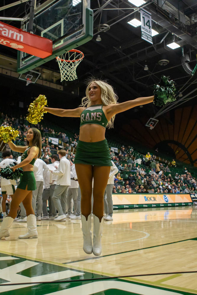 A cheerleader jumps with her arms out to the side during a sports game.