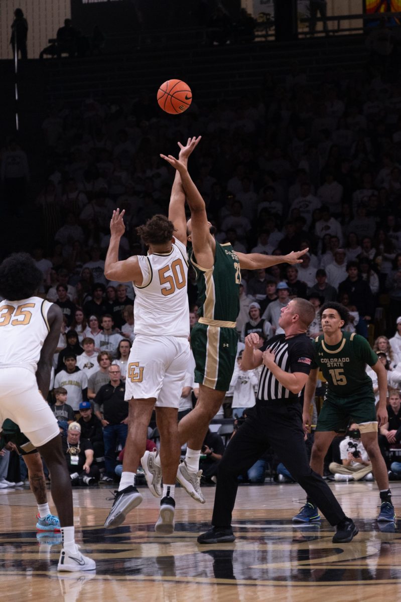 A player in a green and gold uniform and a player in a white and gold uniform jump to grab the orange basketball