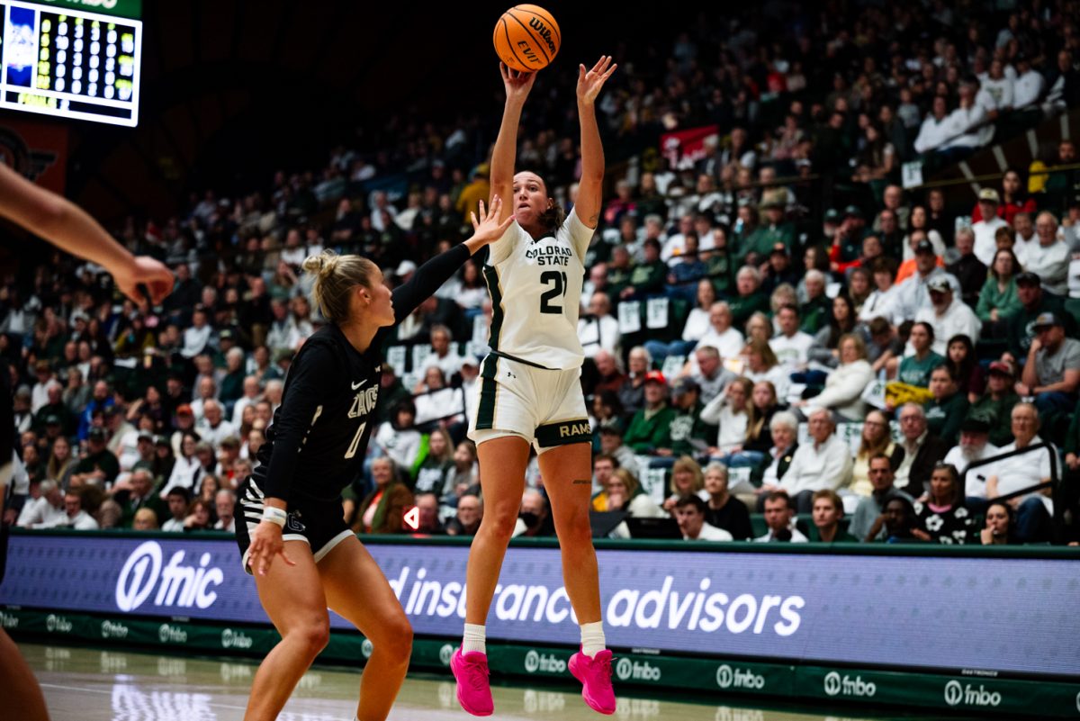 A female basketball player in white and green jumps with a basketball. A defensive player in black and white guards her.