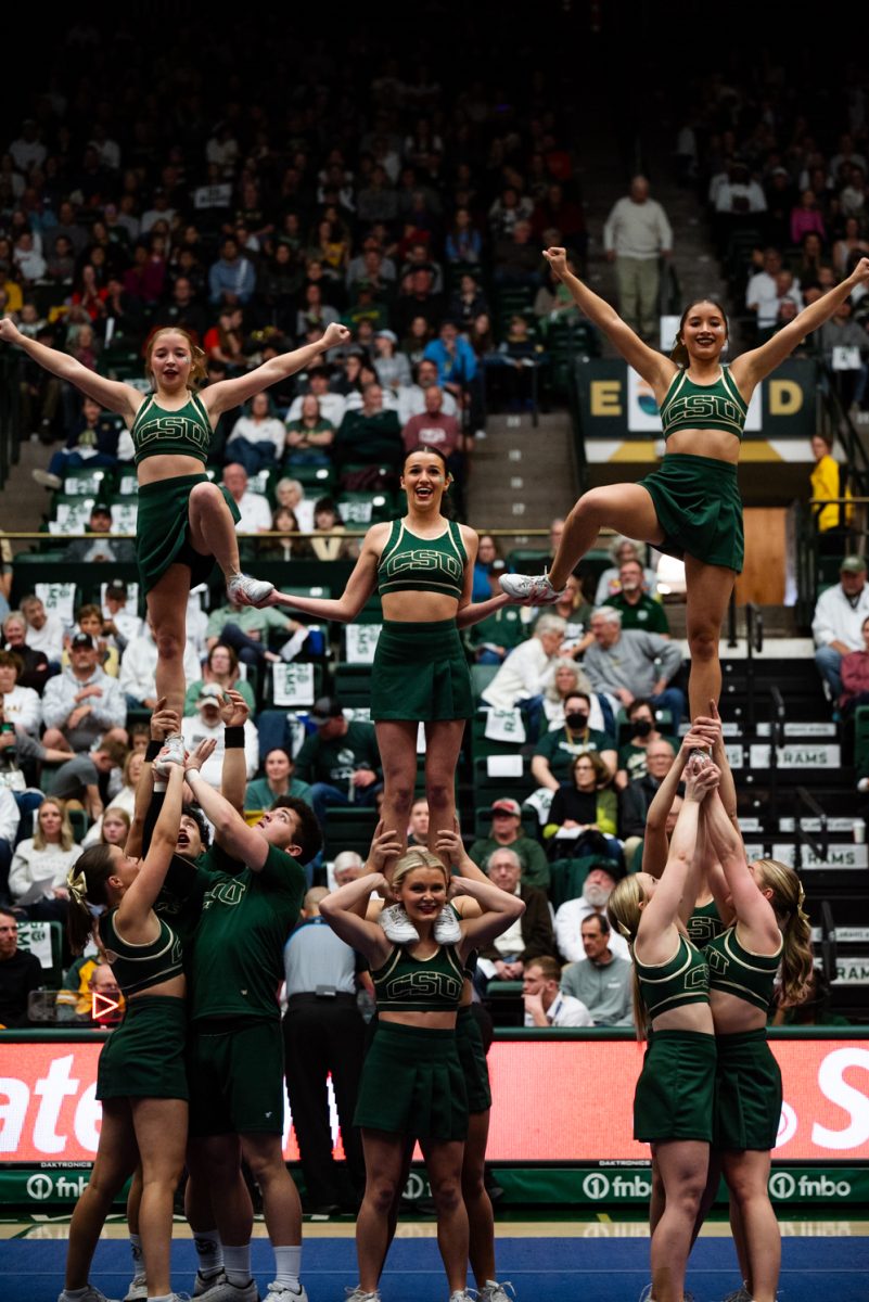 A group of cheerleaders in green and gold. Three are lifted in the air, smiling, with the rest holding them.