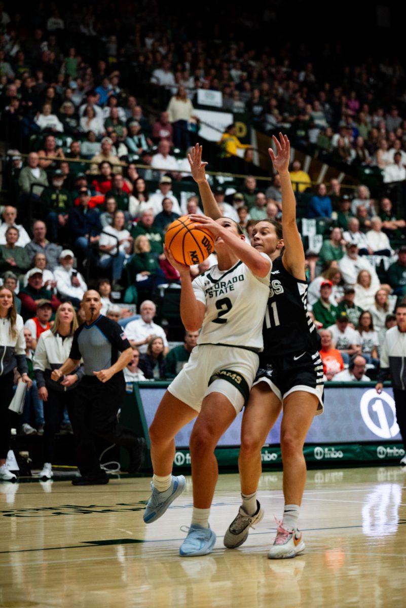 A female basketball player in white and green starts to jump to shoot the ball in her hands. A player in black and white raises her hands behind her.