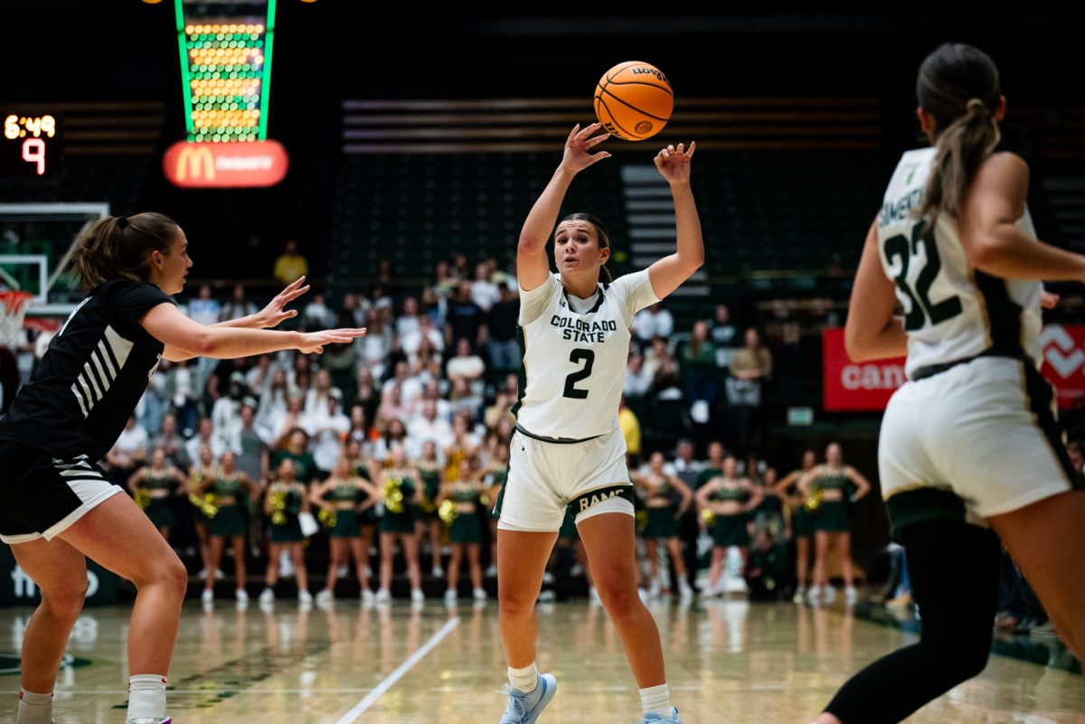 A female basketball player in white and green passes the ball to her teammate.