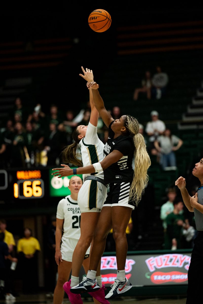 Two female basketball players jump up for a basketball. One on the left is in white and green and the other is in black and white.