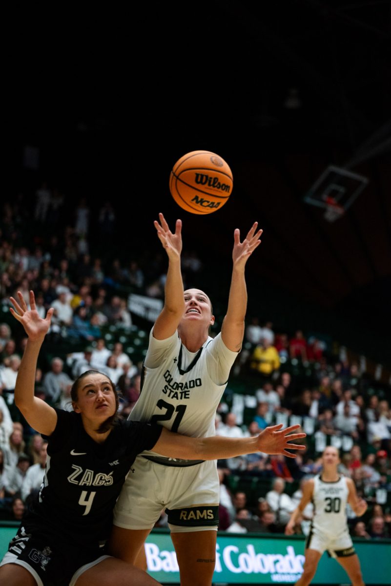 A female basketball player in white and green reaches for a basketball while a player in black and white tries to block her.